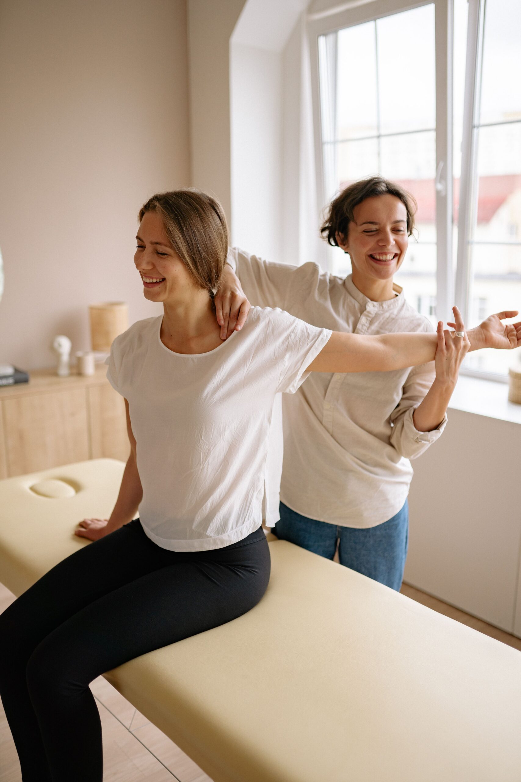 About A therapist guides a woman in a stretching exercise on a massage table in a clinic setting.