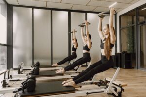 Service-2-min Three women synchronously practicing Pilates on reformers in a modern gym studio.