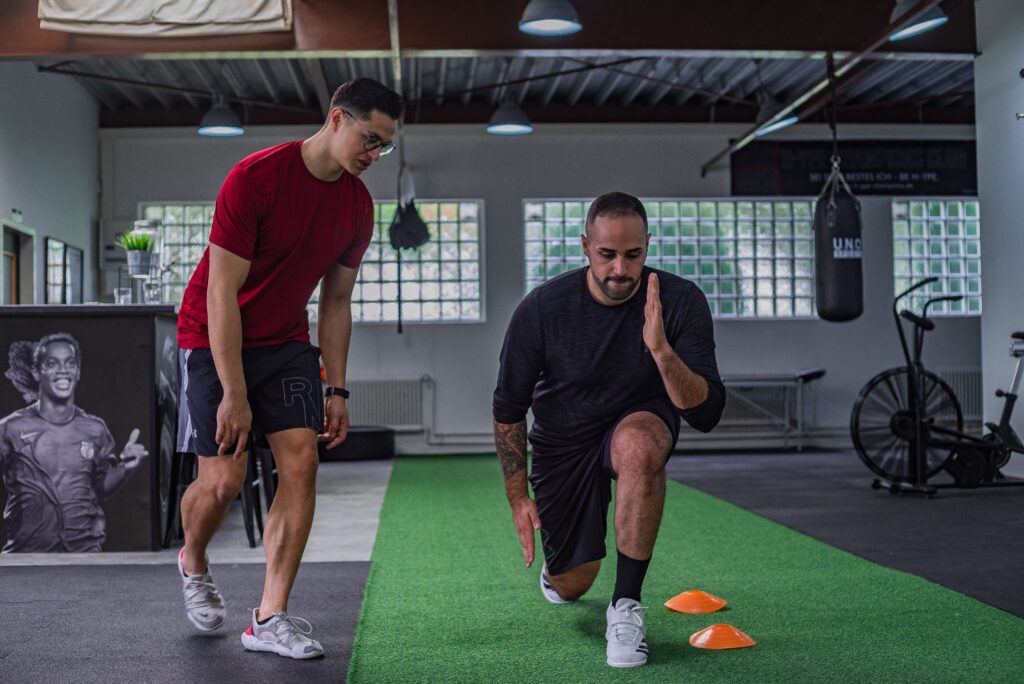 Fisioterapia Deportiva Full body of focused man in sportswear doing stretching exercises with coach in contemporary fitness center